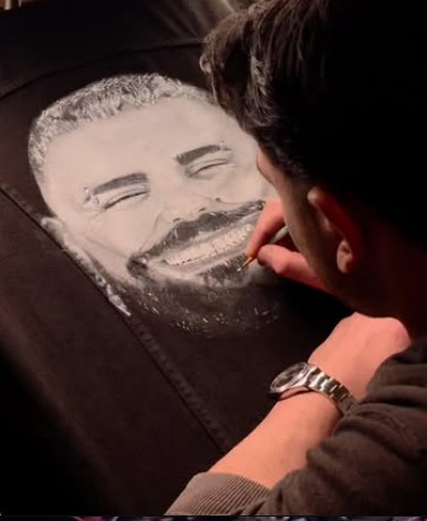 Gianni painting a realistic portrait on the back of a black denim jacket